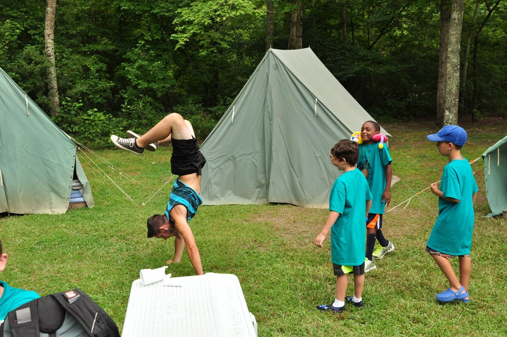 Three young campers watch an adolescent male camper doing a handstand.