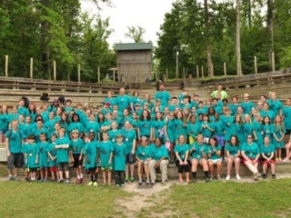 Group of campers wearing teal t-shirts standing in an amphitheater.
