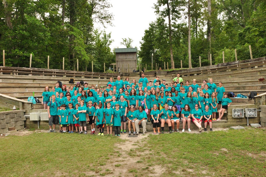 Group of campers wearing teal t-shirts standing in an amphitheater.