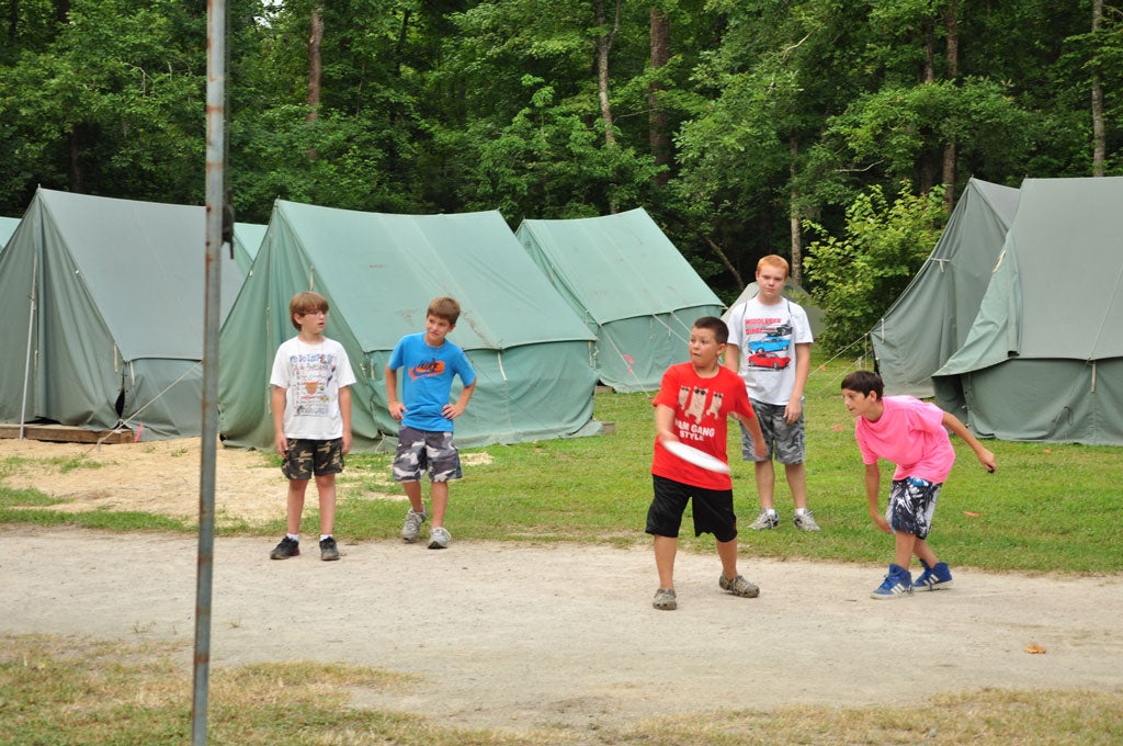 A group of young male campers playing with a frisbee.