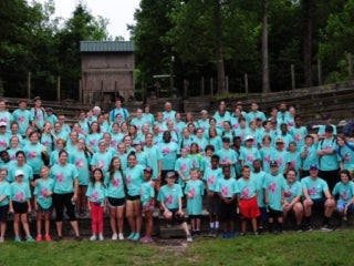A group of campers wearing light aqua t-shirts stands in an amphitheater.
