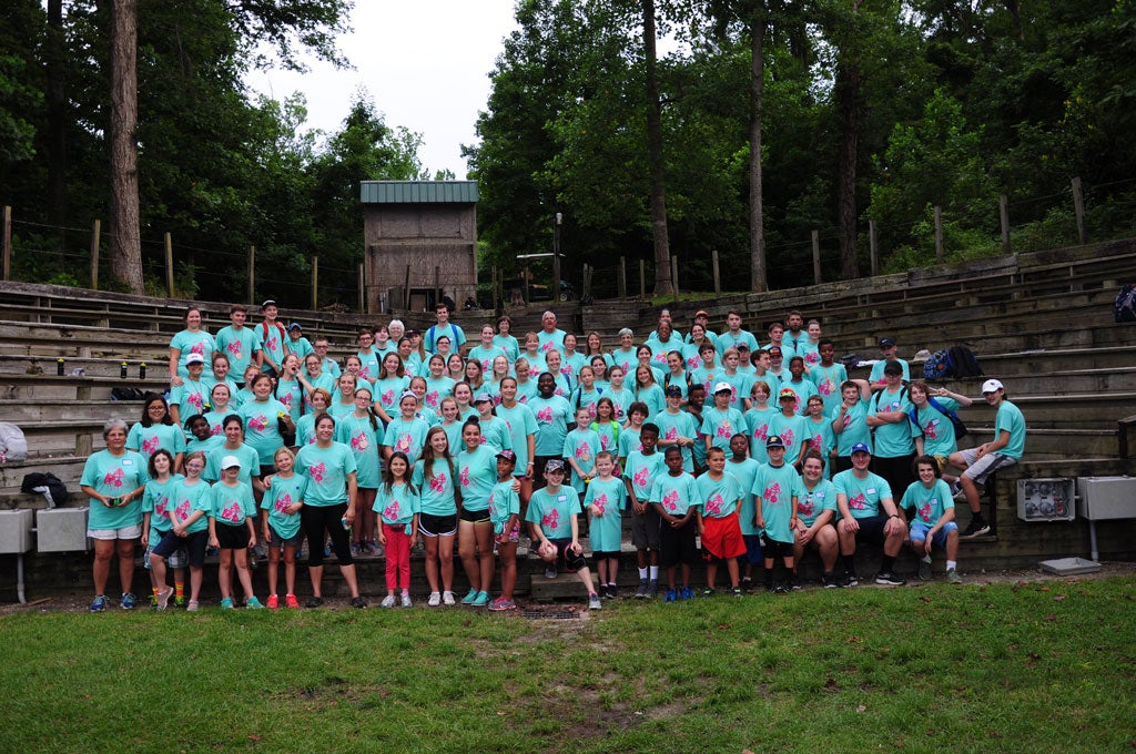 A group of campers wearing light aqua t-shirts stands in an amphitheater.