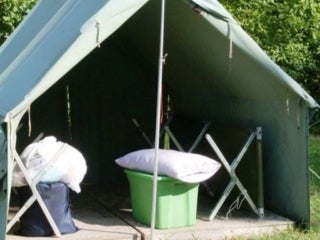A green tent with a plastic tub, pillow, and a couple bags inside.