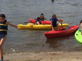 A group of campers on the edge of a body of water with kayaks and paddle boards.