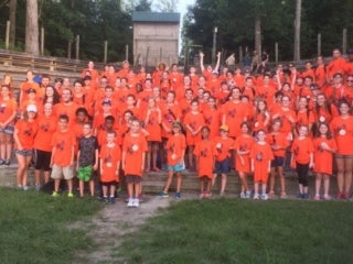 A group of campers wearing bright orange t-shirts standing in an amphitheater.