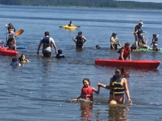 Group of campers in a body of water playing with kayaks and paddle boards.