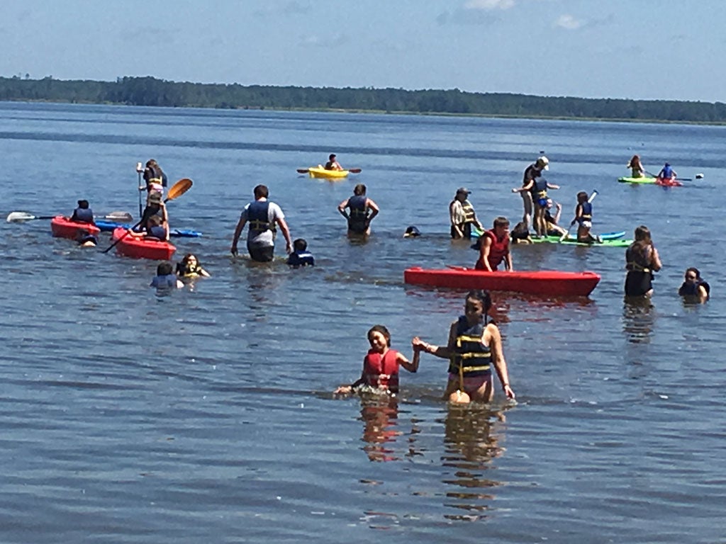 Group of campers in a body of water playing with kayaks and paddle boards.