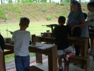 Group of campers standing at a line of gun rests pointing long BB guns down a range.