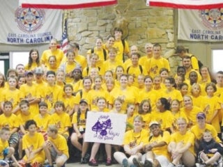 Group of campers in yellow t-shirts holding a Camp Needles In The Pines poster.