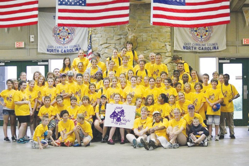 Group of campers in yellow t-shirts holding a Camp Needles In The Pines poster.
